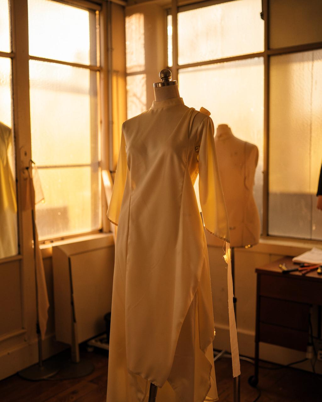 Tailor draping cream silk on a dress form in a golden-hour atelier